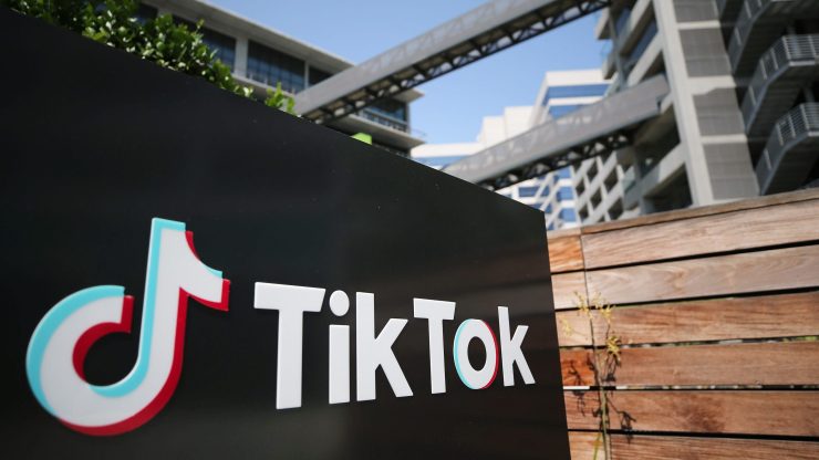 A sign with the TikTok logo in front of an office complex.