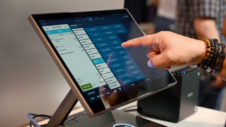 A finger points to a POS system on a tablet.