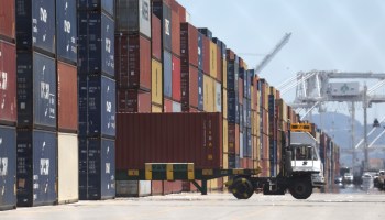 A truck driver pulls out hauling a shipping container amid stacks of shipping containers at the Port of Oakland.