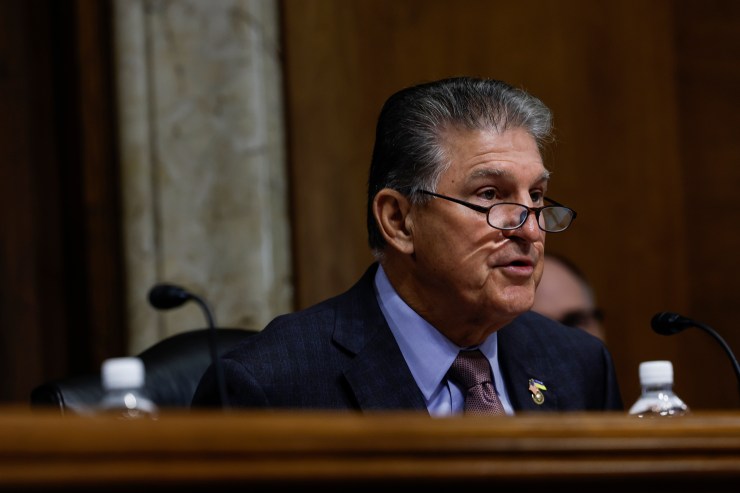 Sen. Joe Manchin (D-WV) seated behind a wooden desk, speaking into a microphone.