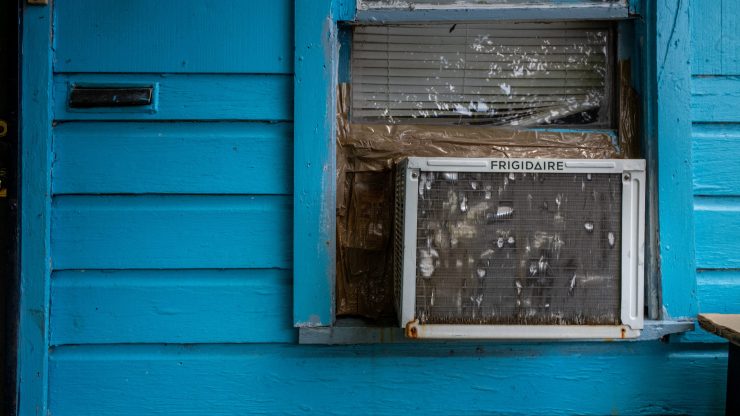 An air conditioner taped into the window of a blue-sided house.