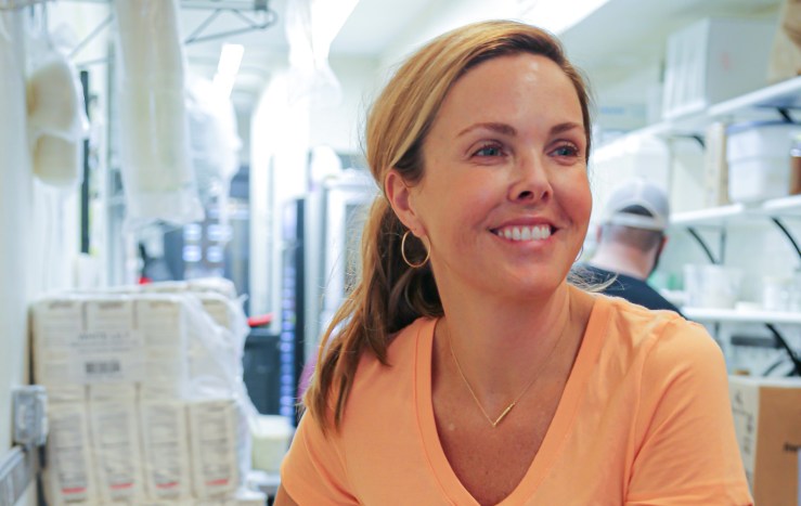 Carrie Morey, smiling and wearing an orange shirt, stands in the back of a restaurant.
