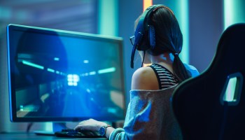 A girl in a gaming chair with a headset on plays a video game.