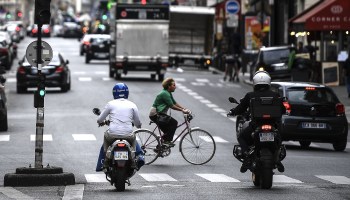 A woman rides a bicycle past motorcyclists in Paris.