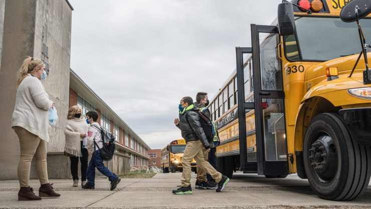 Teachers greet students getting off the school bus.