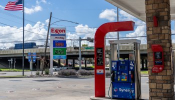 Gas prices are displayed at an Exxon gas station with an American flag in the background.