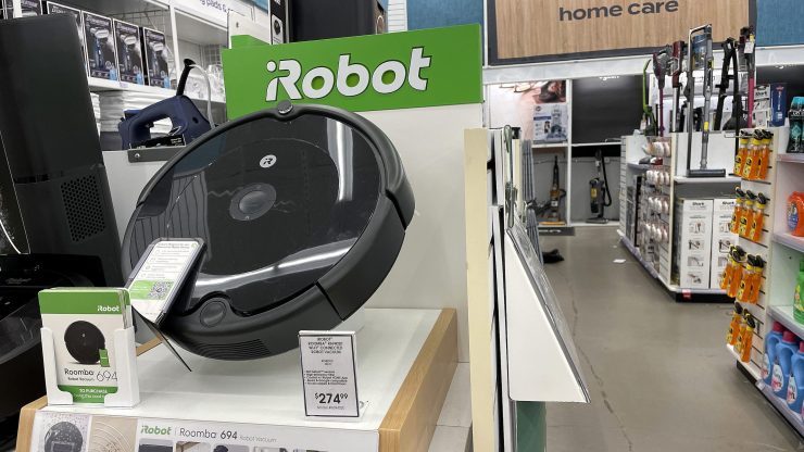 A Roomba vacuum cleaner on display in a store, beneath an iRobot sign