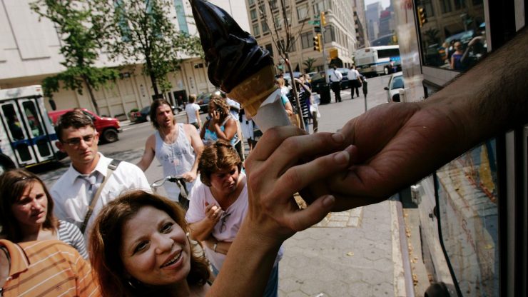 A woman reaches for an ice cream cone from a truck. It's a hot day and a line forms behind her.
