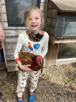 A young boy (Kiel) is holding a brown chicken in his hands while smiling. 