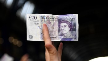 A customer holds out a 20-pound note, featuring the face of Queen Elizabeth II.