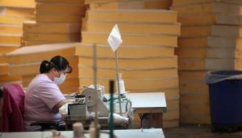 A woman sews in a warehouse space for outdoor furniture manufacturing.