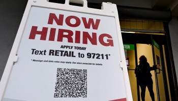 A woman walks past a "Now Hiring" sign in front of a store on January 13, 2022 in Arlington, Virginia.