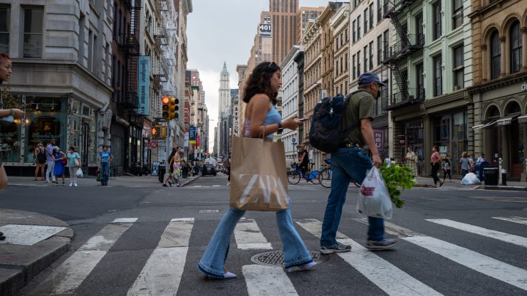 A woman holding a Zara shopping bag crosses the street