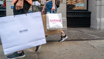 Pedestrians carry shopping bags displaying the names of boutiques.