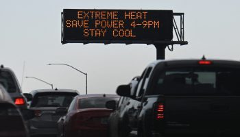 Vehicles drive past an electronic sign that reads: "Extreme heat, save power 4-9pm, stay cool."