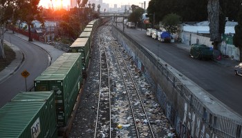 A freight train passes along a section of track littered with trash.