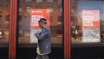 A man in a hat walks by a long, empty storefront in New York.