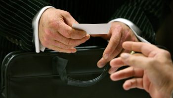A businessperson hands another person a business card.