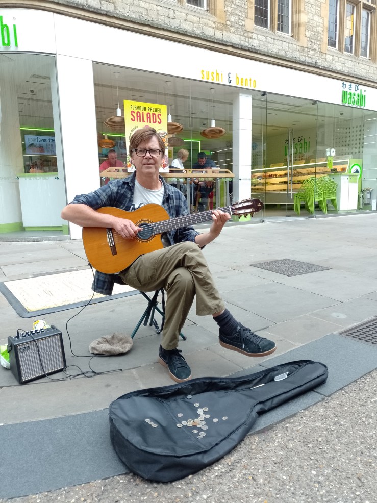 Musician Neil Mason performs on a sidewalk with his guitar.