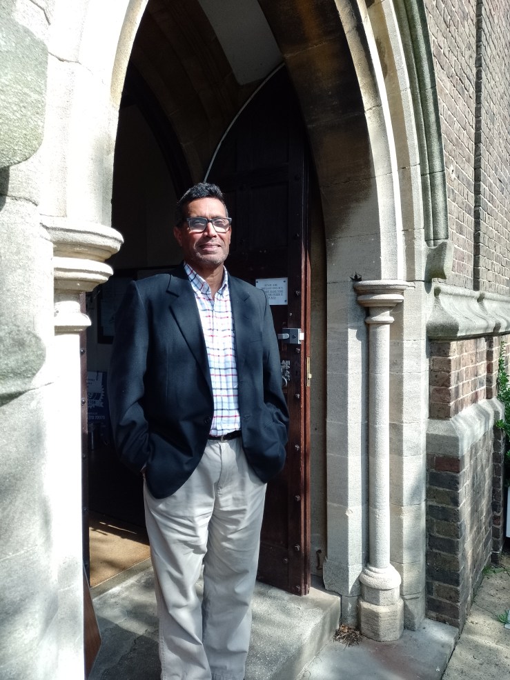 Father Felix Mascarenhas, vicar of the Church of the Good Shepherd, stands in a church doorway.