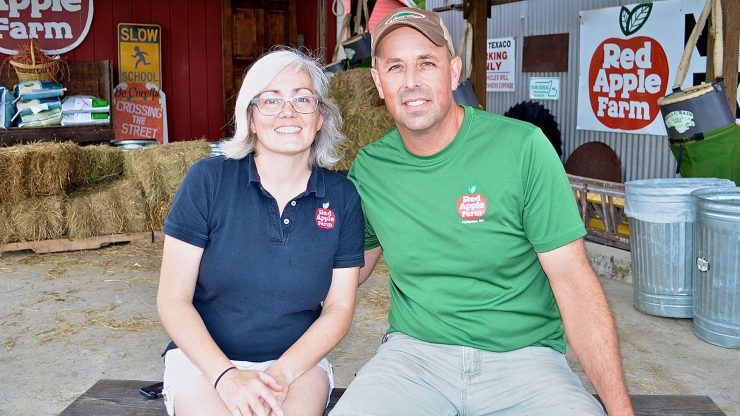 Two people in Red Apple Farms logo T-shirts sit side by side in a barn.