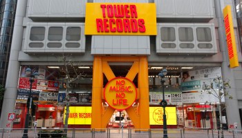 The exterior of Tower Records' major store. On a big sign, in bright red, reds "Tower Records" in front of a yellow background. Slightly below, within a circle, is Tower Records' motto, "No Music, No Life" in similar colors.