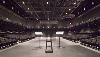 An empty black box theater with a stool and two music stands on the stage