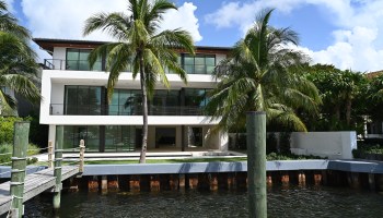 Modern waterfront mansion in Coconut Grove, faced with windows, with palm trees in the foreground.
