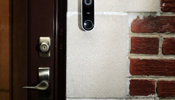 A Ring smart video camera placed next to the front door of a house.