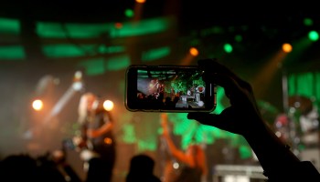 L7's performance is viewed through a phone camera, with the live band out of focus in the background.