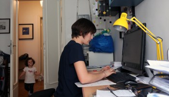 A woman working at her computer with a small child in the room.