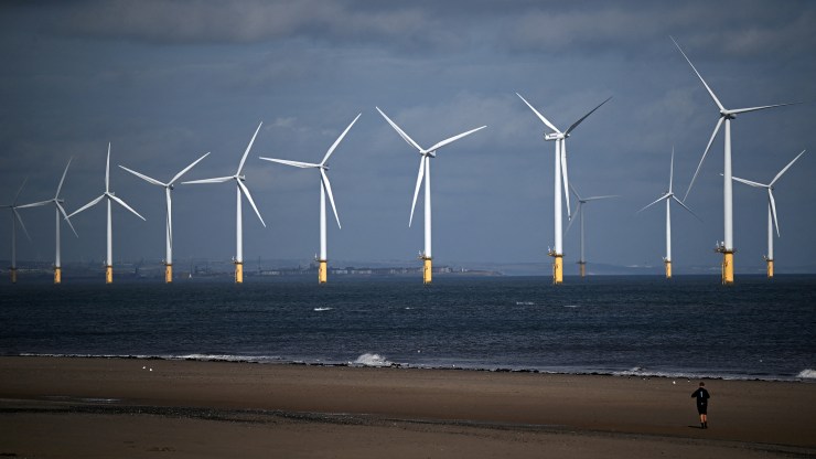 A person walks along the beach backdropped by wind turbines of EDF Energy Renewables' Teesside Wind Farm, off the coast of Redcar in north east England on September 7, 2022.
