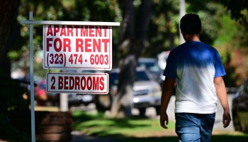 A person walks past an apartment for rent sign on a tree-lined street in South Pasadena, California.