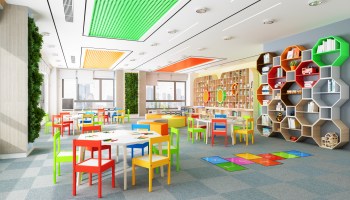 An empty kindergarten classroom complete with small, multicolored tables and chairs for children, along with toys and decorations.