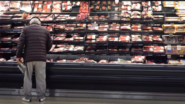 A man stands in front of a meat display at a grocery store.