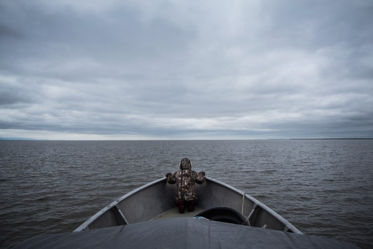 NEWTOK, AK - JULY 01: Samuel John sits at the bow of his father's boat while heading out to go salmon fishing on July 1, 2015 in Newtok, Alaska. Newtok has a population of approximately of 375 ethnically Yupik people and was established along the shores of the Ninglick River, near where the river empties into the Bering Sea, by the Bureau of Indian Affairs (BIA) in 1959. The Yupik people have lived on the coastal lands along the Bering Sea for thousands of years. As global temperatures rise the village is being threatened by the melting of permafrost, greater ice and snow melt and larger storms from the Bering Sea. According to the U.S. Army Corp of Engineers, the highest elevated point in Newtok - the school - could be underwater by 2017. Approximately nine miles away, Mertarvik has been established, though families have been slow to relocate to the new village. (Photo by Andrew Burton/Getty Images)