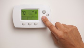A person uses their index finger to press a button on a digital thermostat, which reads 78 degrees Fahrenheit.