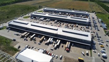 An aerial view of an industrial warehouse with cars and trucks parked outside.