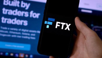 This illustration photo shows a smart phone screen displaying the logo of FTX, the crypto exchange platform, with a screen showing the FTX website in the background.