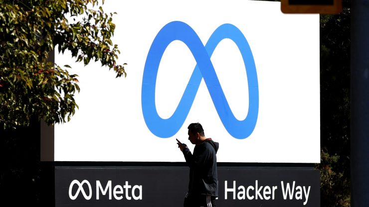 A man walks in front of a new Meta logo in front of the company's headquarters.