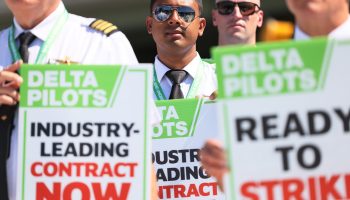 Closeup of pilots on a picket line with signs that says "Industry-leading contract now" and "ready to strike"