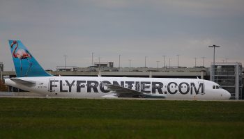 An airplane on the ground that says "FLYFRONTIER.COM" on its side.
