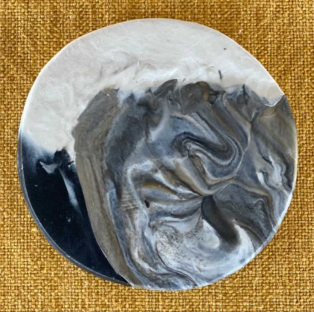 A clay coaster with swirls of white, black, gray and brown.