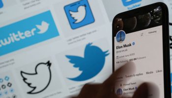 Elon Musk's Twitter page displayed on the screen of a smartphone with Twitter logos in the background.