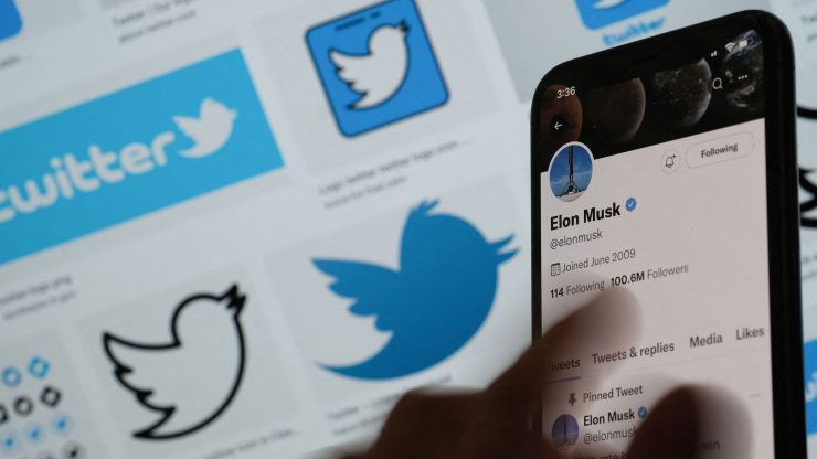 Elon Musk's Twitter page displayed on the screen of a smartphone with Twitter logos in the background.