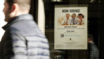 A 'now hiring' sign is displayed in a window of a store