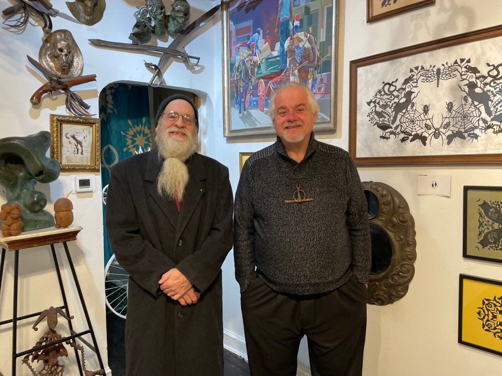 ศิลปิน Geoffrey Harris และ Jim Pollock ยืนอยู่หน้าผนังที่ปกคลุมด้วยงานศิลปะในห้องหน้าบ้านของ Pollock