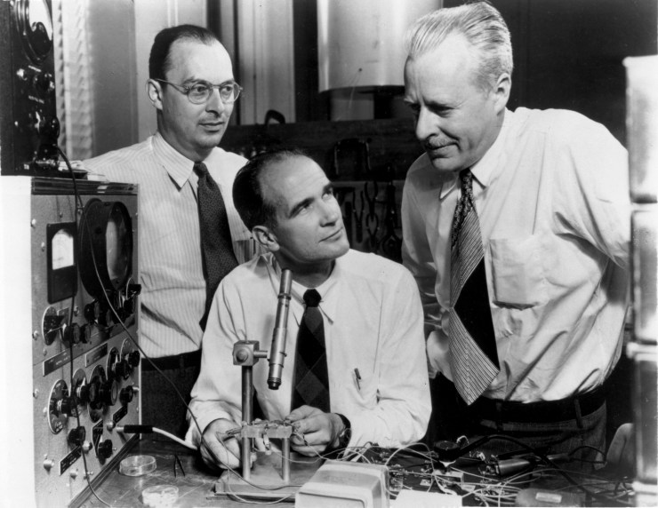 Three physicists in shirts and ties in Bell Laboratories in 1948. There's a microscope in the middle of the photo pointed at a transistor.