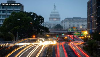 A picture of the U.S. capitol. A light streak from cars lights up the highway in front