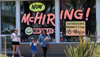 A family walks past a McDonald's restaurant with "Now McHiring!" painted on the window.